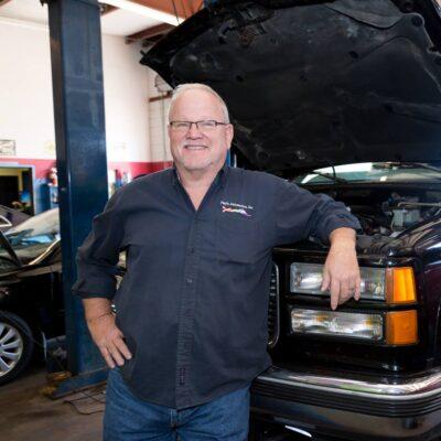 One of the auto repairman under the hood smiling at the camera for a picture